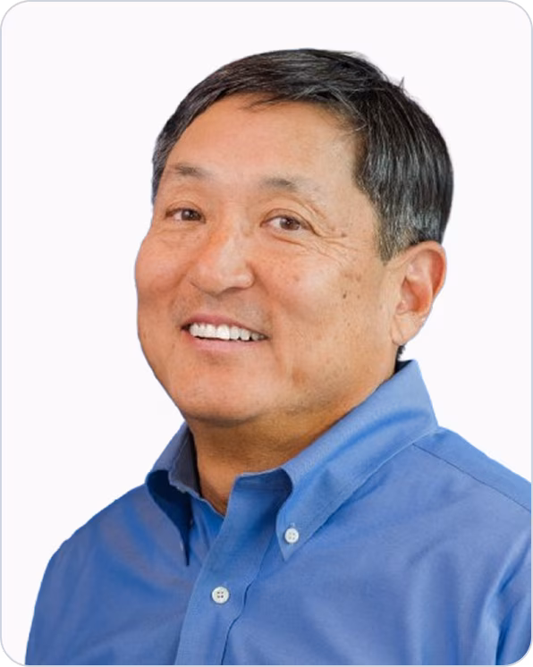 Middle-aged man with short black hair wearing a blue button-up shirt smiling slightly against a white background.