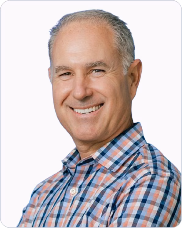 Smiling middle-aged man with short gray hair wearing a blue, orange, and white plaid shirt.