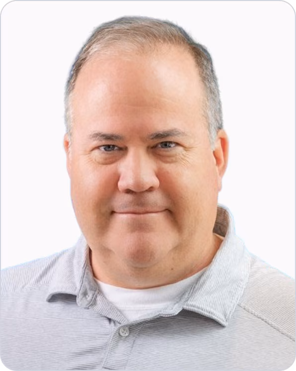 Middle-aged man with light skin and short hair wearing a light gray collared shirt, looking directly at the camera with a neutral expression.