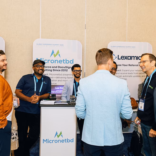 Group of six professionals conversing at a business event booth with Micronetbd branding and promotional materials.