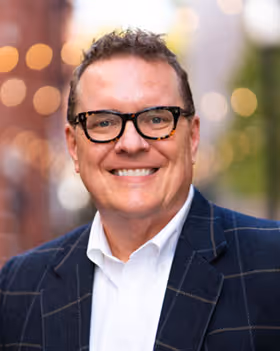 Smiling middle-aged man in a blue button-up shirt looking at the camera.