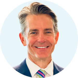 Smiling middle-aged man with gray hair wearing a suit and colorful striped tie against a white background.