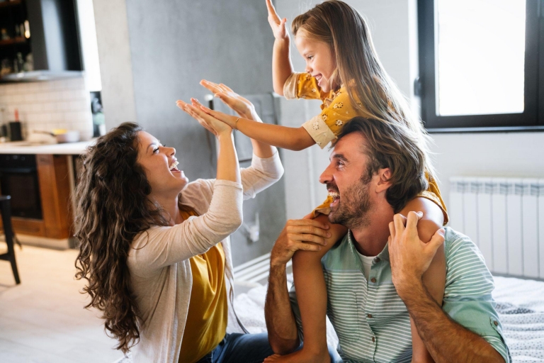 Family playing indoors, child on shoulders giving high-five