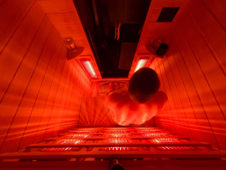 Man sitting in an infrared sauna illuminated by red light therapy panels