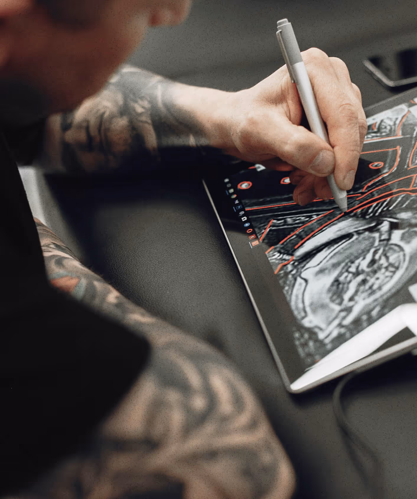 Digital artist drawing on tablet with stylus, tattooed arm in view