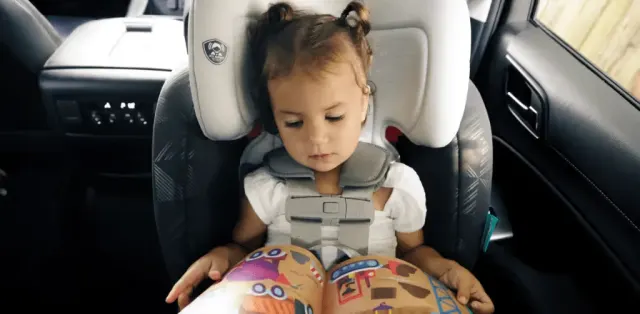 A little girl sitting in a car seat reading a book
