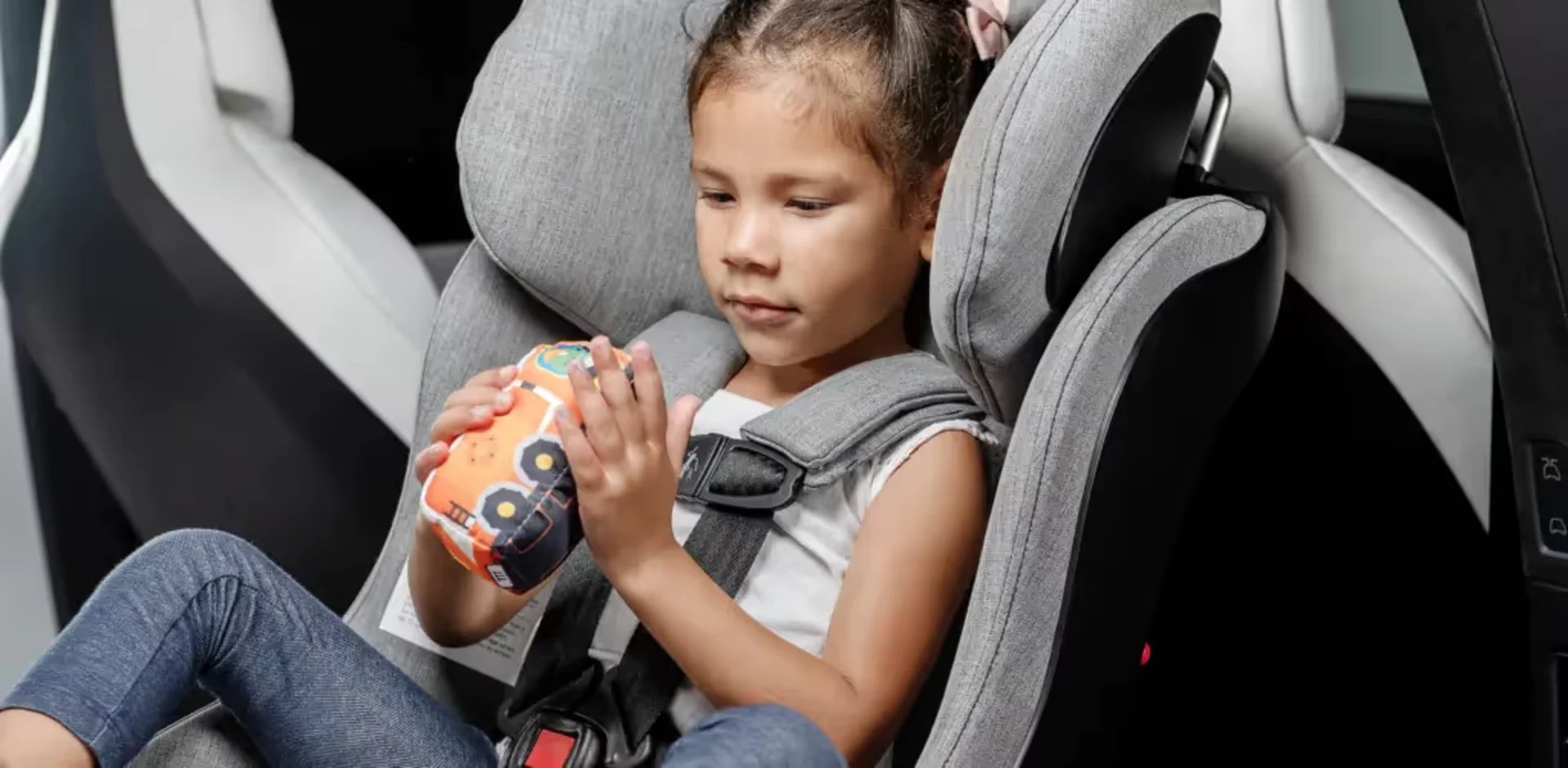A little girl sitting in a car seat holding a toy