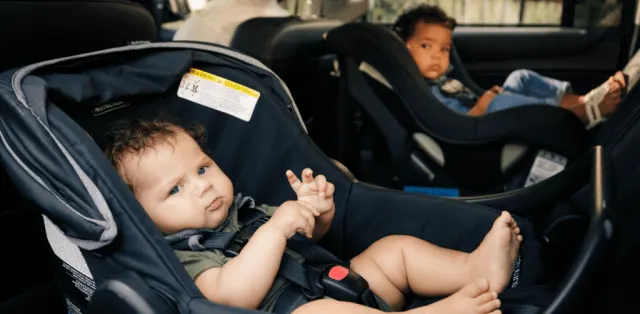 A baby sitting in a car seat next to another child