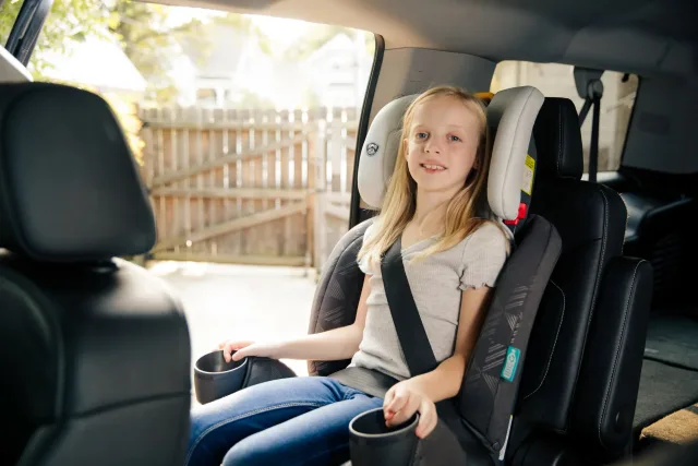 A little girl sitting in a car seat holding a cup