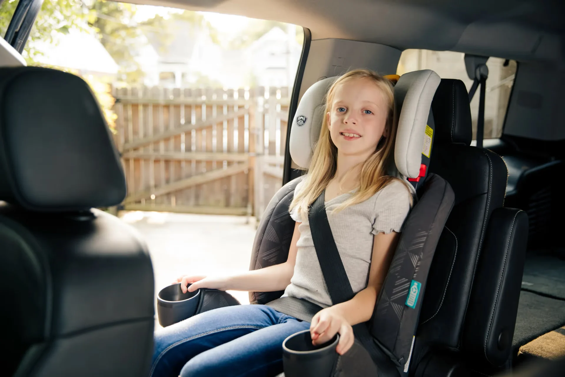 A little girl sitting in a car seat holding a cup