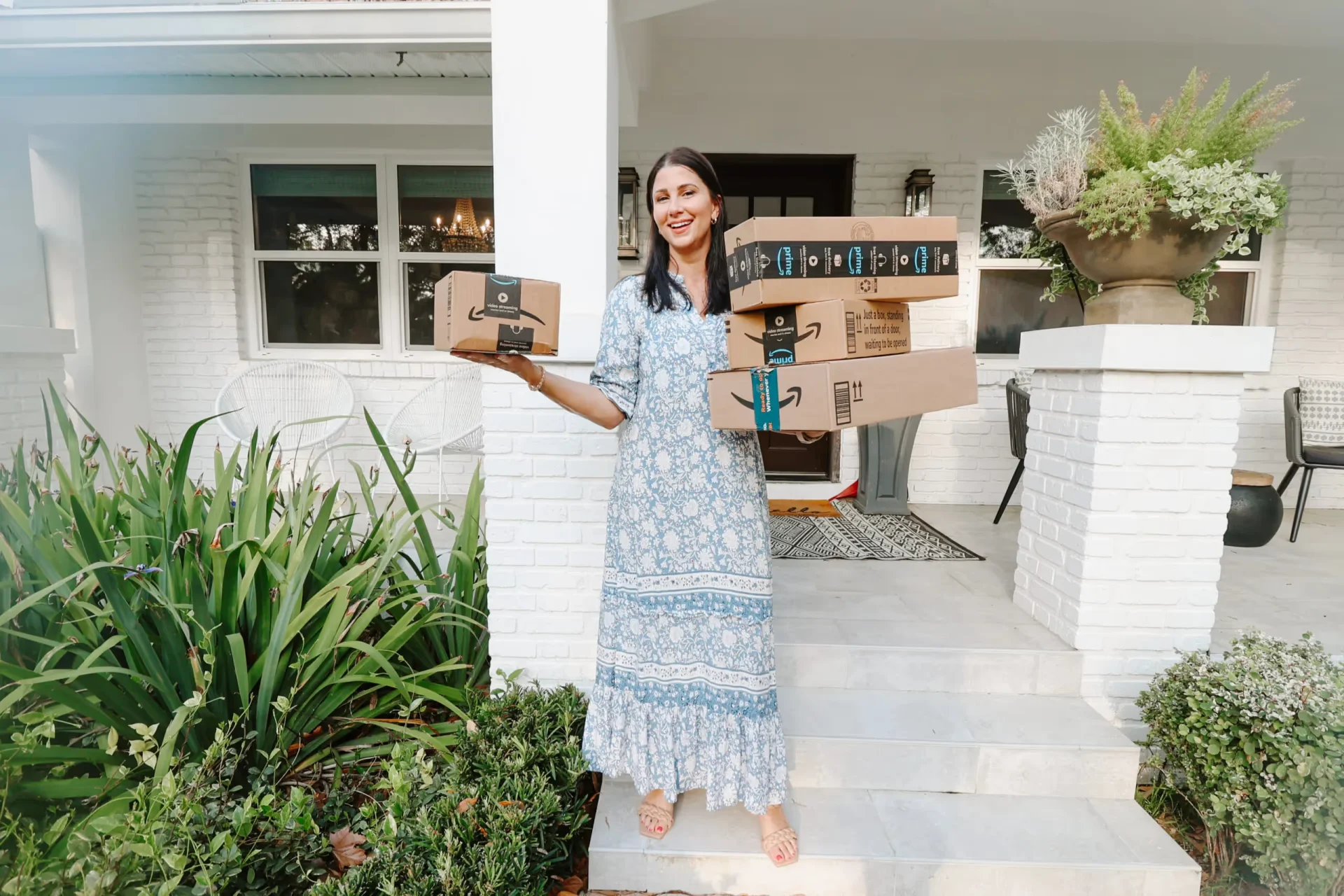 A woman holding a box of pizza in front of a house