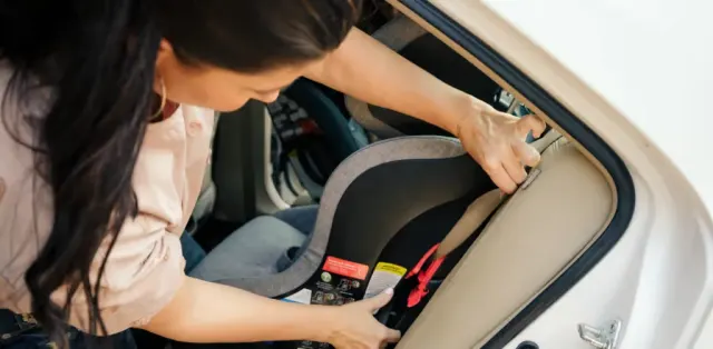 A woman in a pink shirt is putting a seat in a car