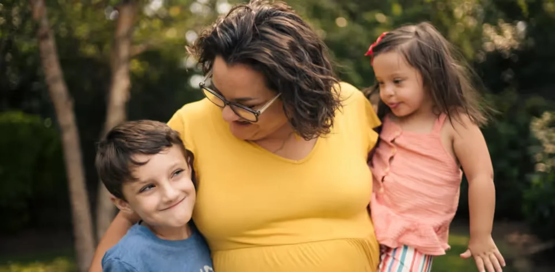 A pregnant woman with two children in a park