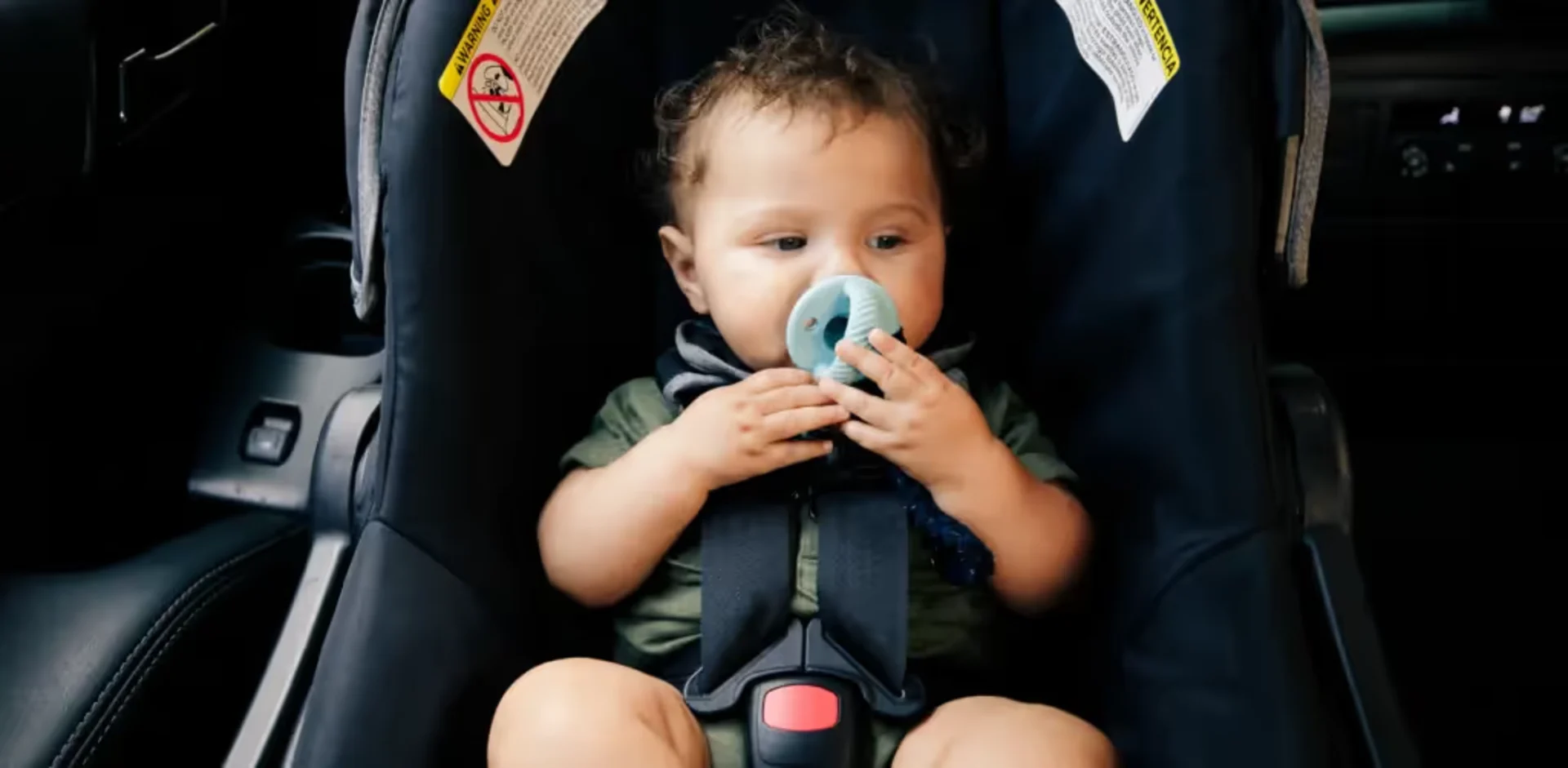 A baby sitting in a car seat with a pacifier in his mouth