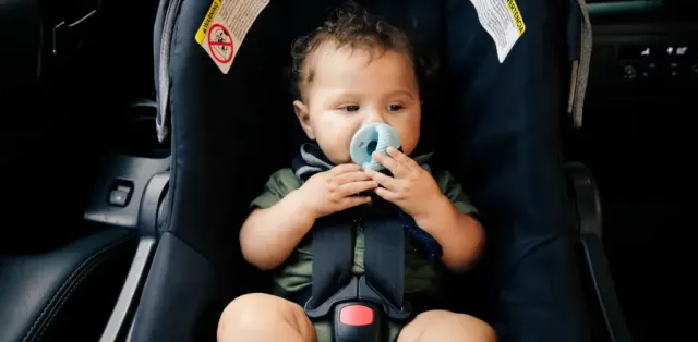 A baby sitting in a car seat with a pacifier in his mouth