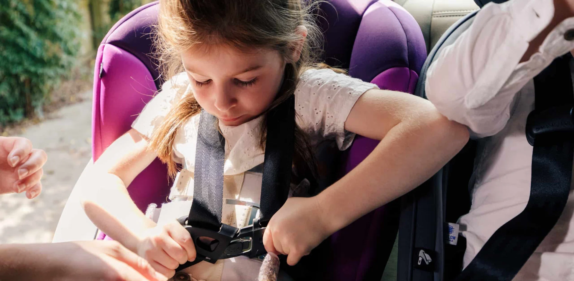 A little girl sitting in a car seat holding a camera