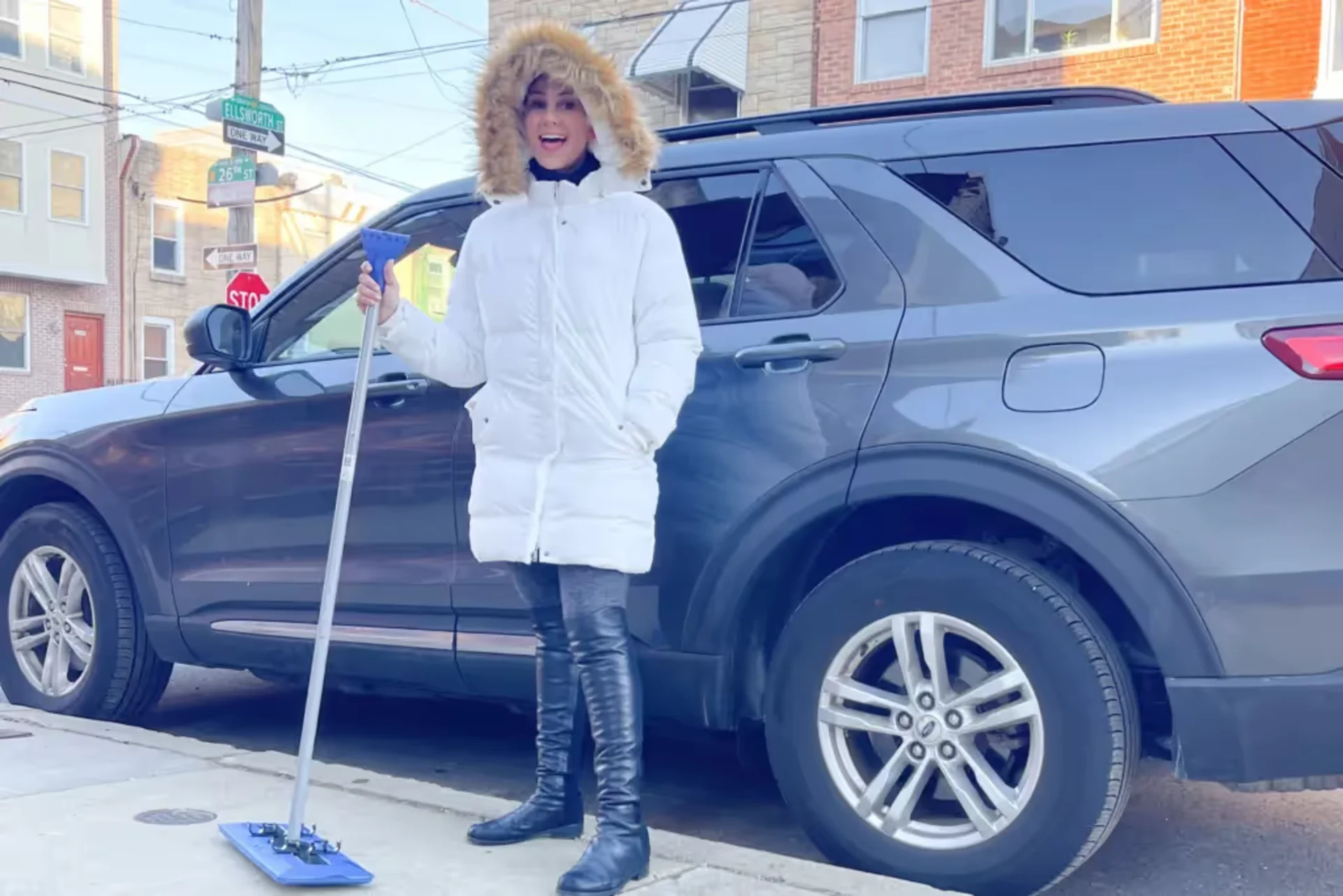 A woman in a white coat is standing in front of a car