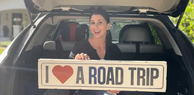 A woman holding a sign that says i love a road trip