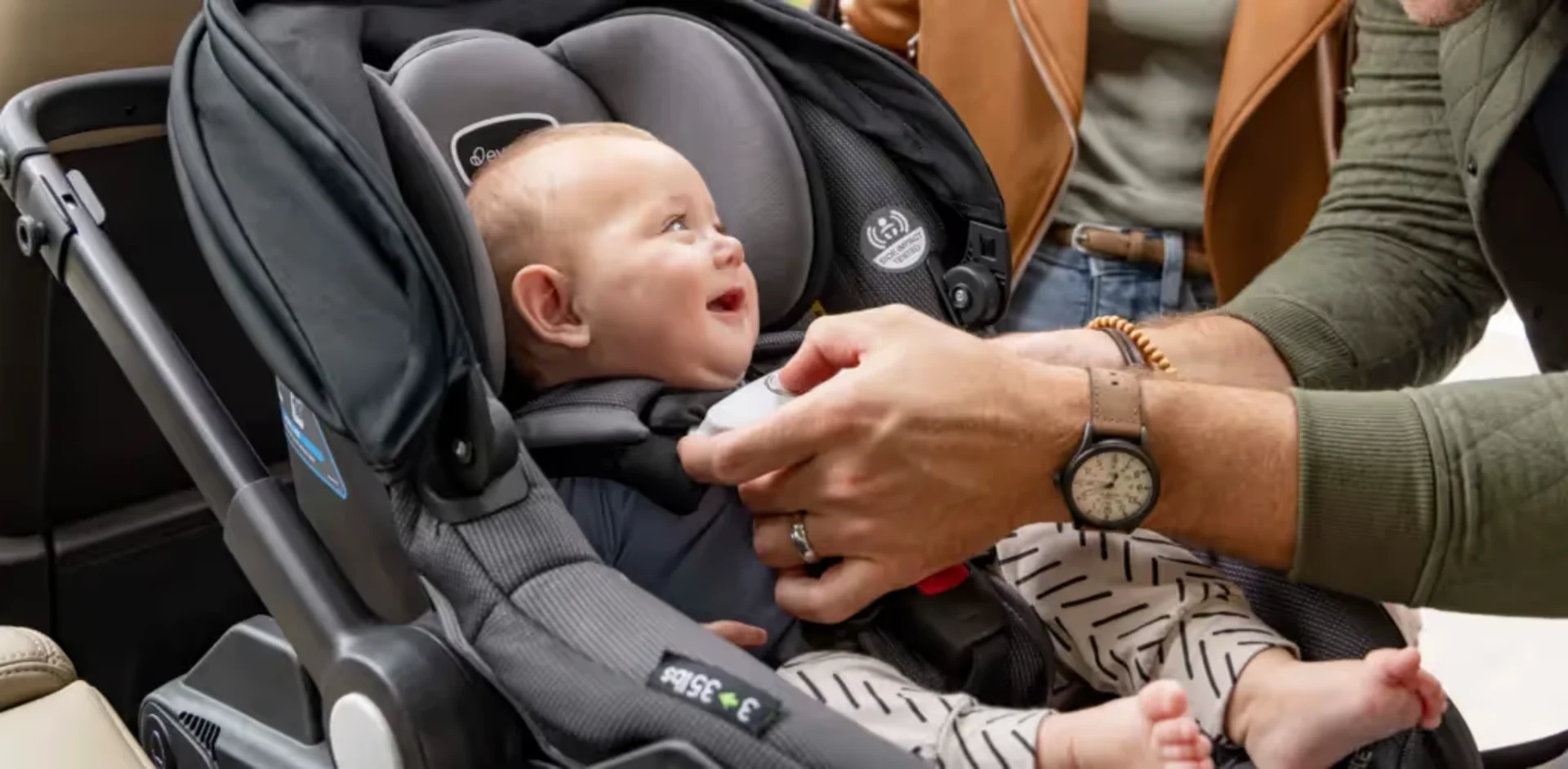 A baby in a car seat being fed by a person
