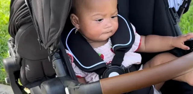 A baby sitting in a stroller looking at the camera