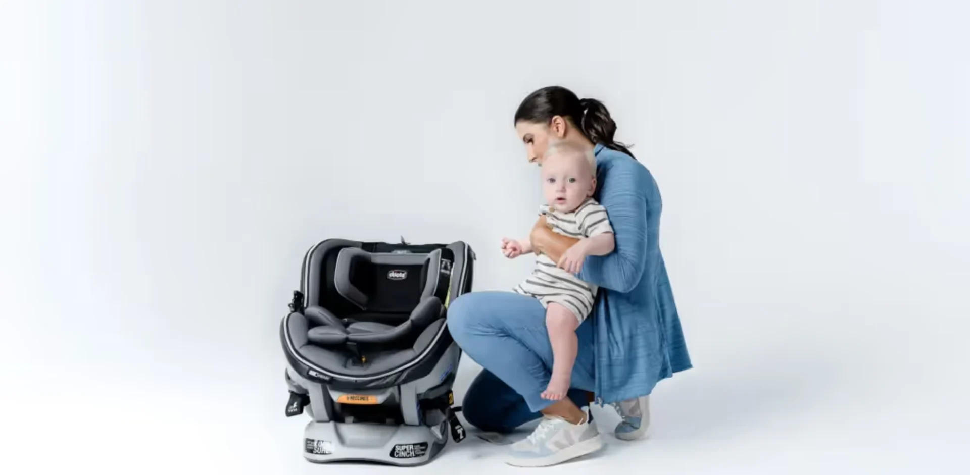 A woman holding a baby next to a car seat