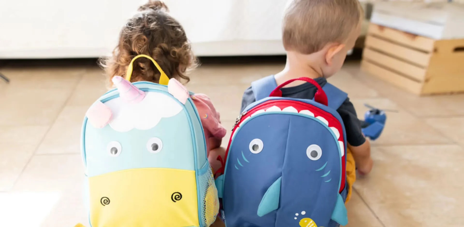 Two children sitting on the floor with backpacks