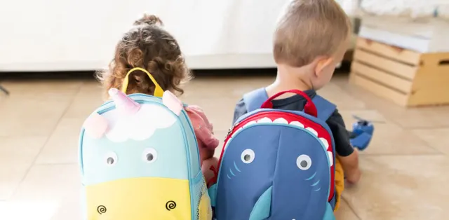 Two children sitting on the floor with backpacks
