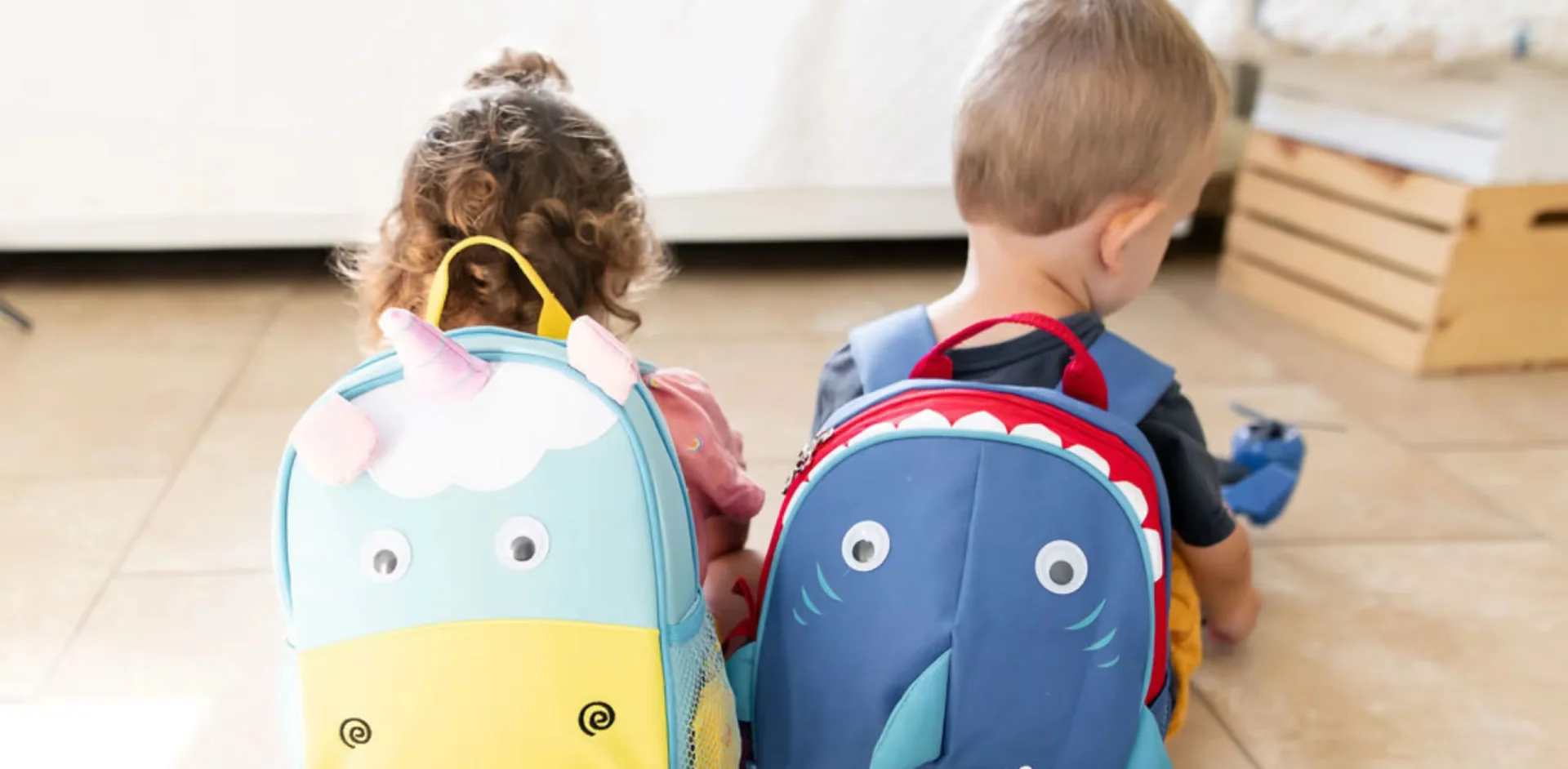 Two children sitting on the floor with backpacks