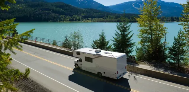 A motor home driving down a road next to a lake