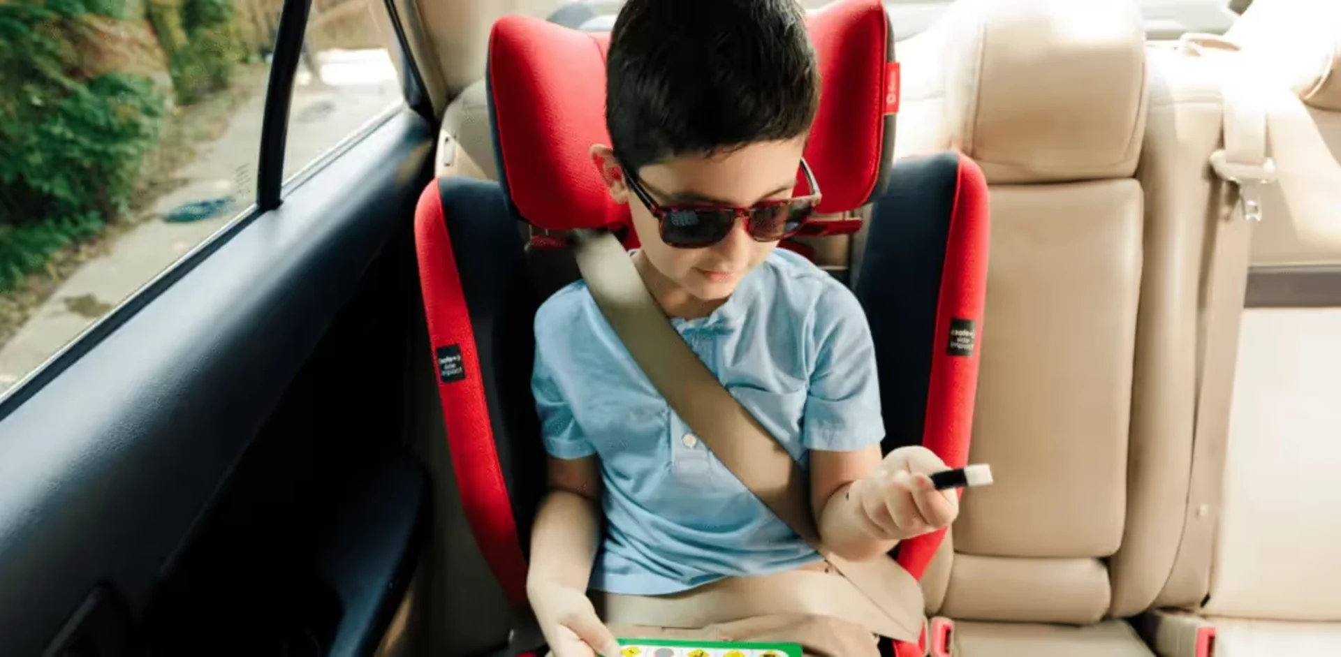 A young boy sitting in a car seat holding a remote control