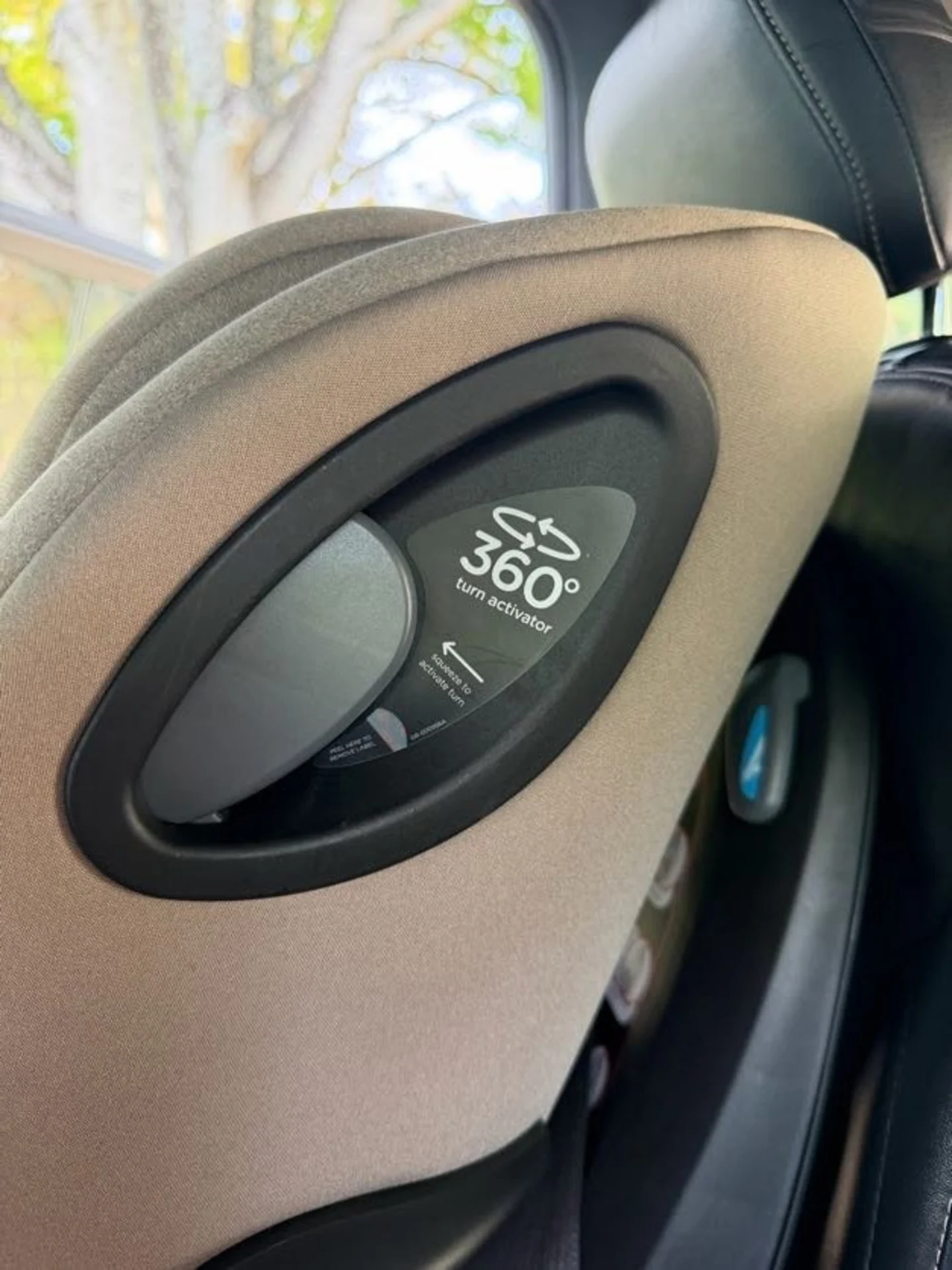 Close-up of the 360-degree turn activator button on the side of a Joie Spin SI car seat in Matcha fabric