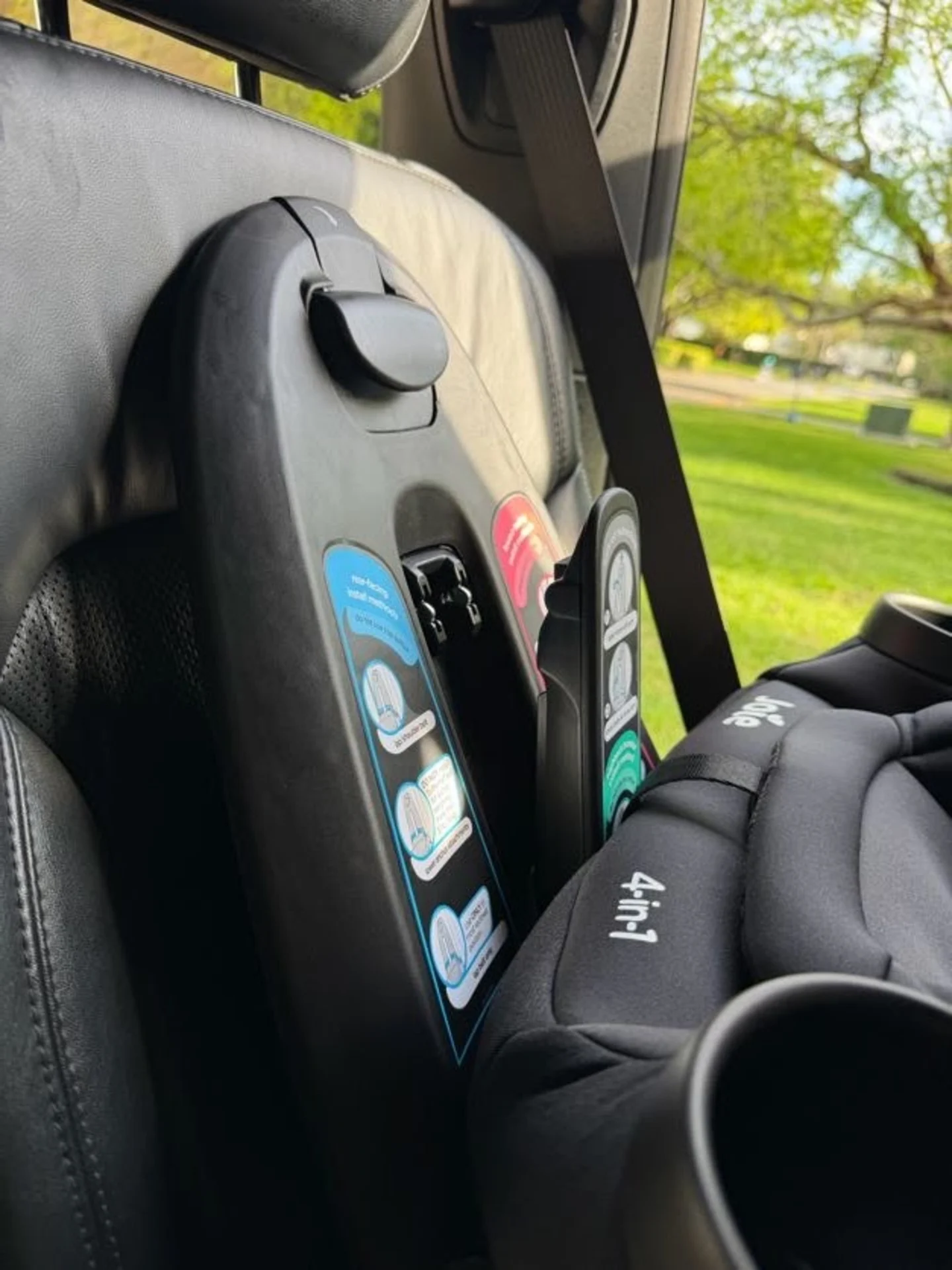 Joie Pepper SI 4-in-1 convertible car seat installed rear-facing in a vehicle with black leather interior and green park view