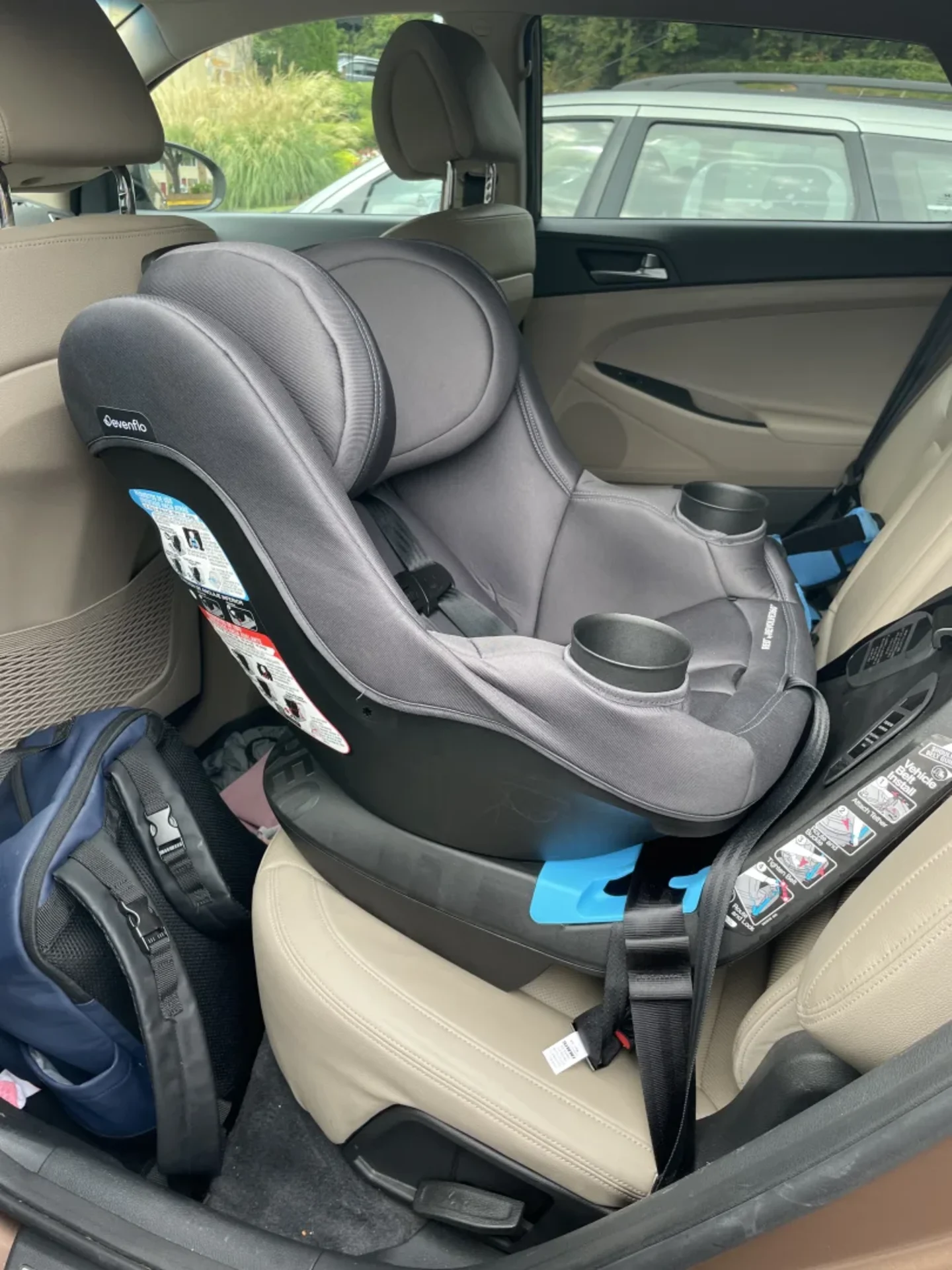 Evenflo REO by Revolve360 convertible car seat in dark gray installed rear-facing on beige leather back seat of a sedan