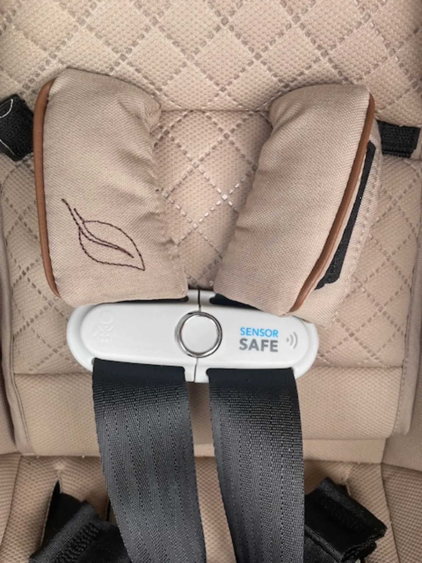 Close-up of the SensorSafe chest clip buckle on the Evenflo Revolve180 Litemax NXT car seat with beige quilted fabric