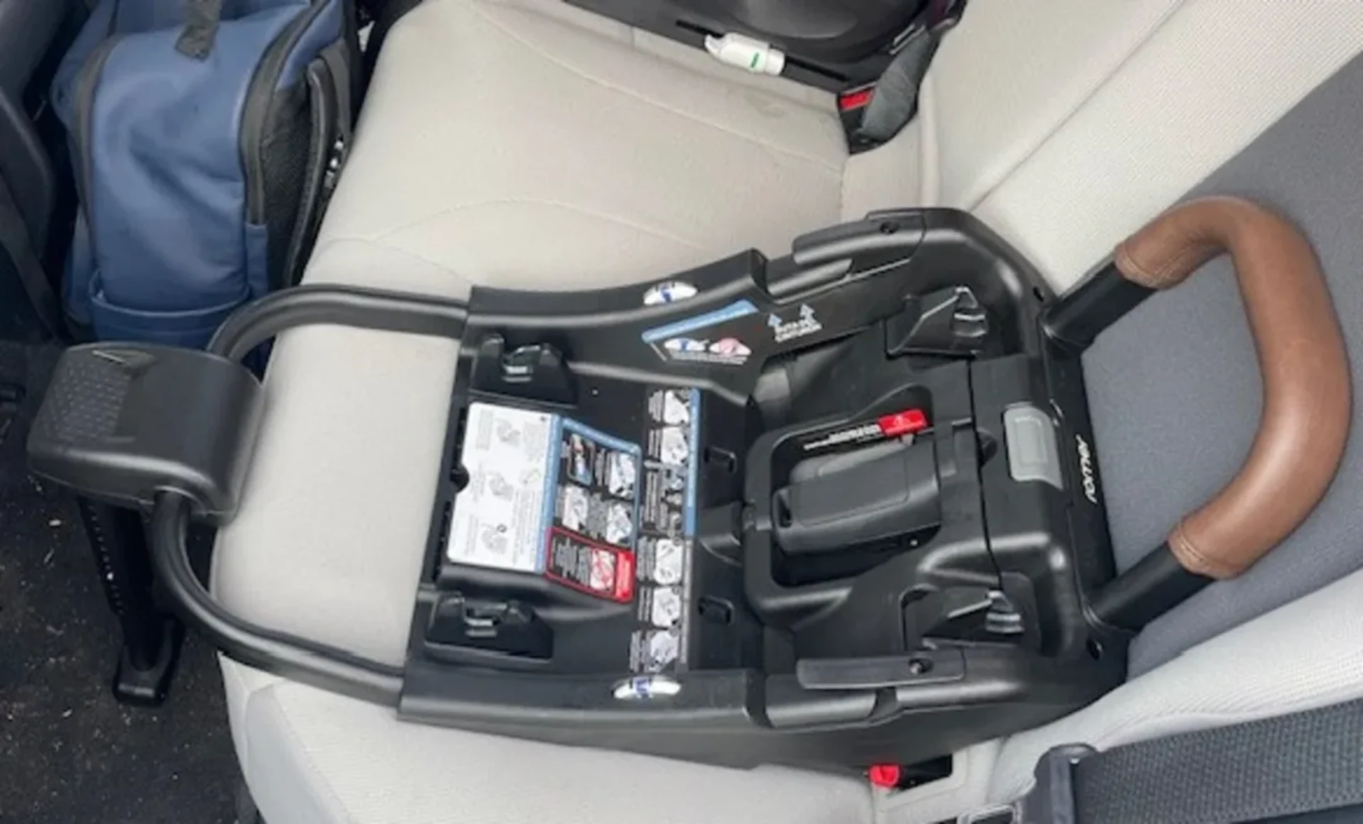 Black Römer Juni infant car seat base placed on beige rear car seat showing installation labels and LATCH connectors