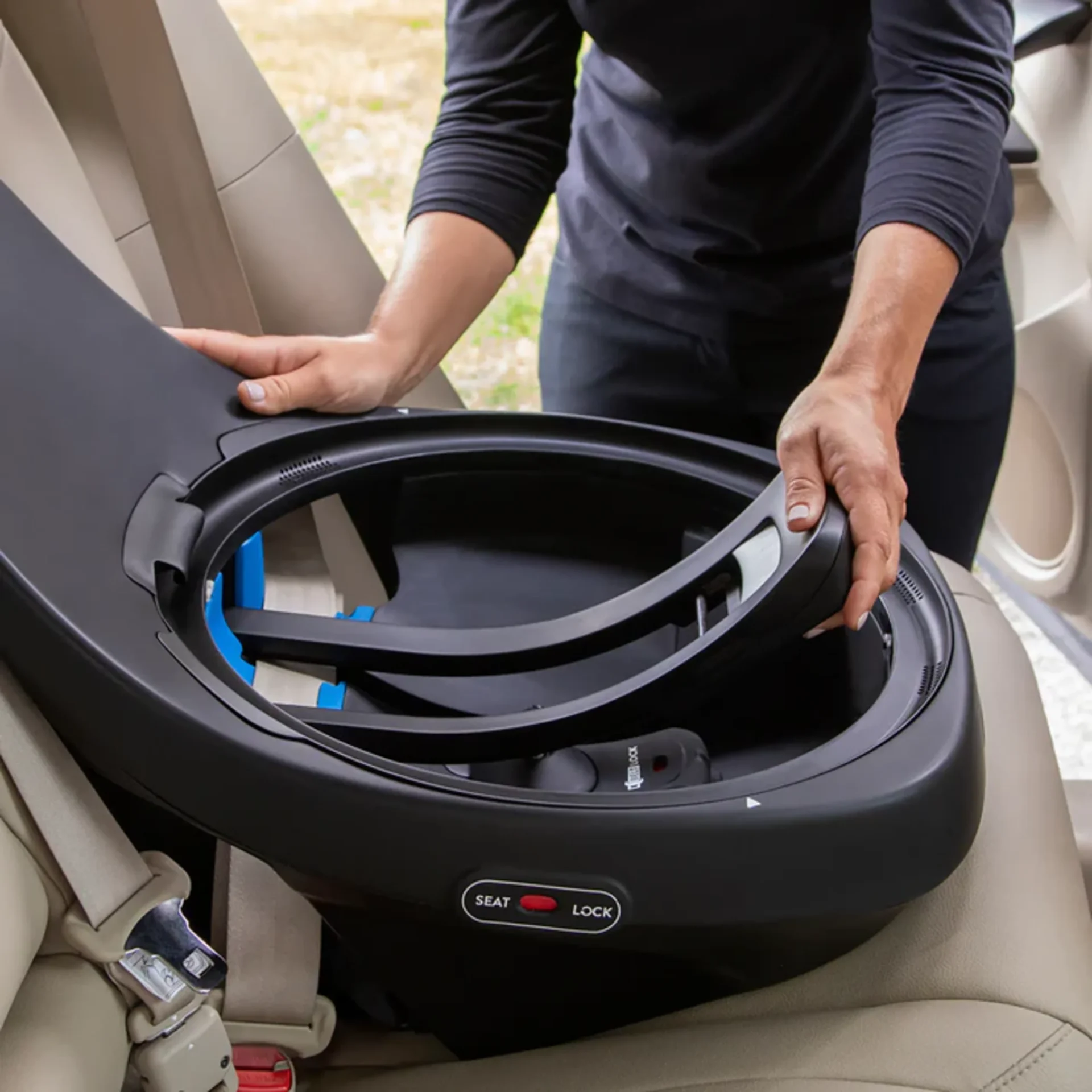 Person installing the Evenflo Revolve rotating car seat base onto a beige vehicle rear seat with seat lock indicator visible