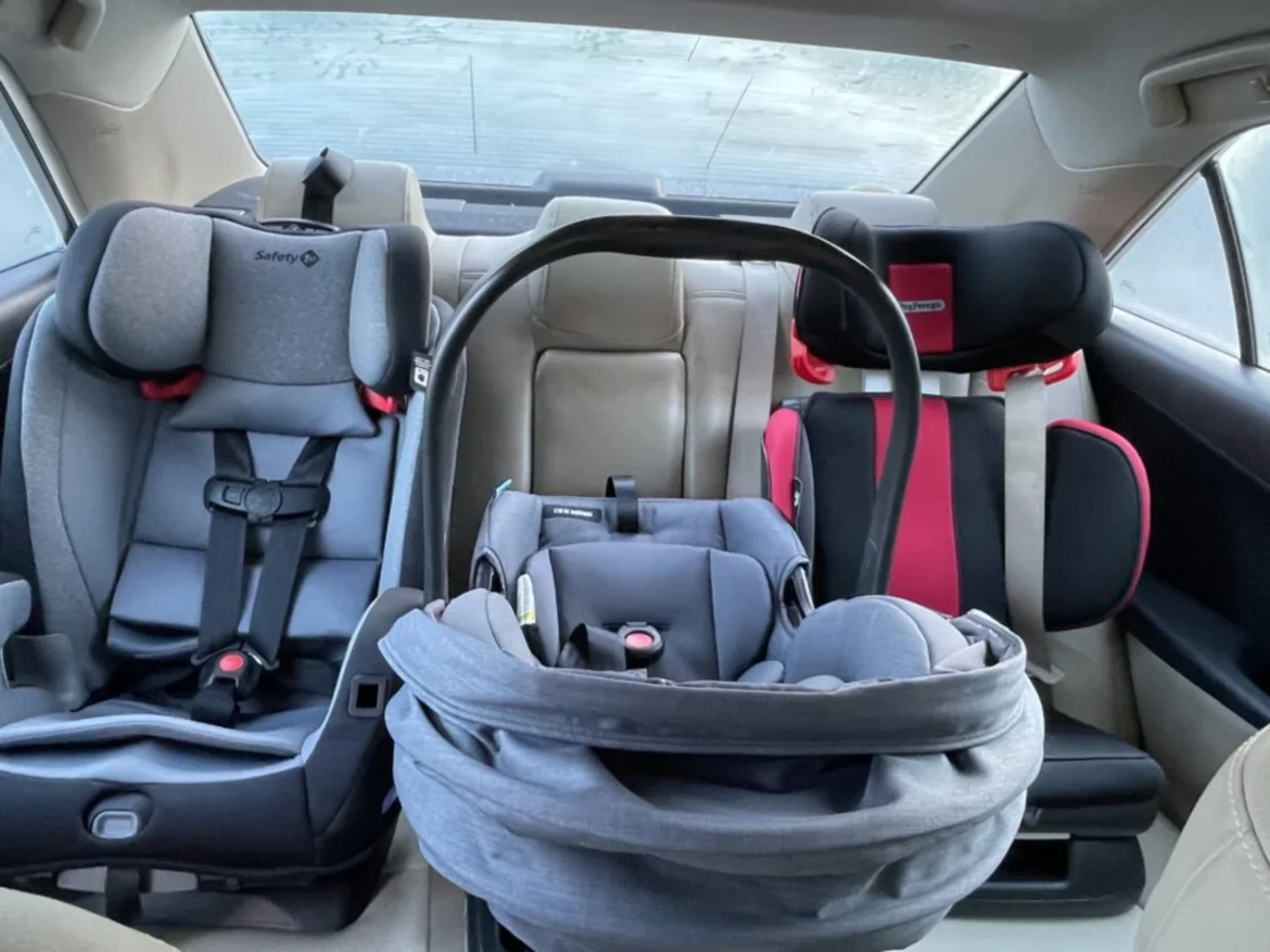 Three child car seats installed across the back seat of a sedan including a PEG Perego Viaggio Flex in red and black on the r