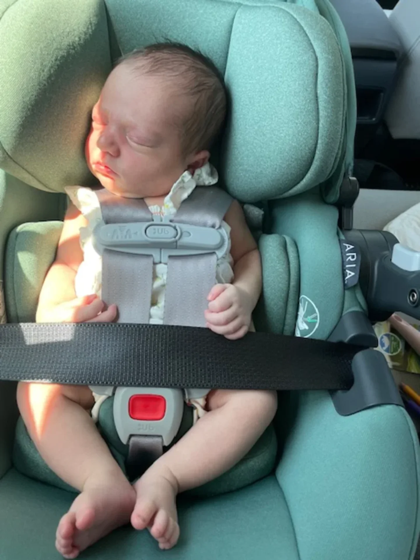 Peaceful newborn baby sleeping securely in a teal UPPAbaby Aria infant car seat with grey five-point harness buckled