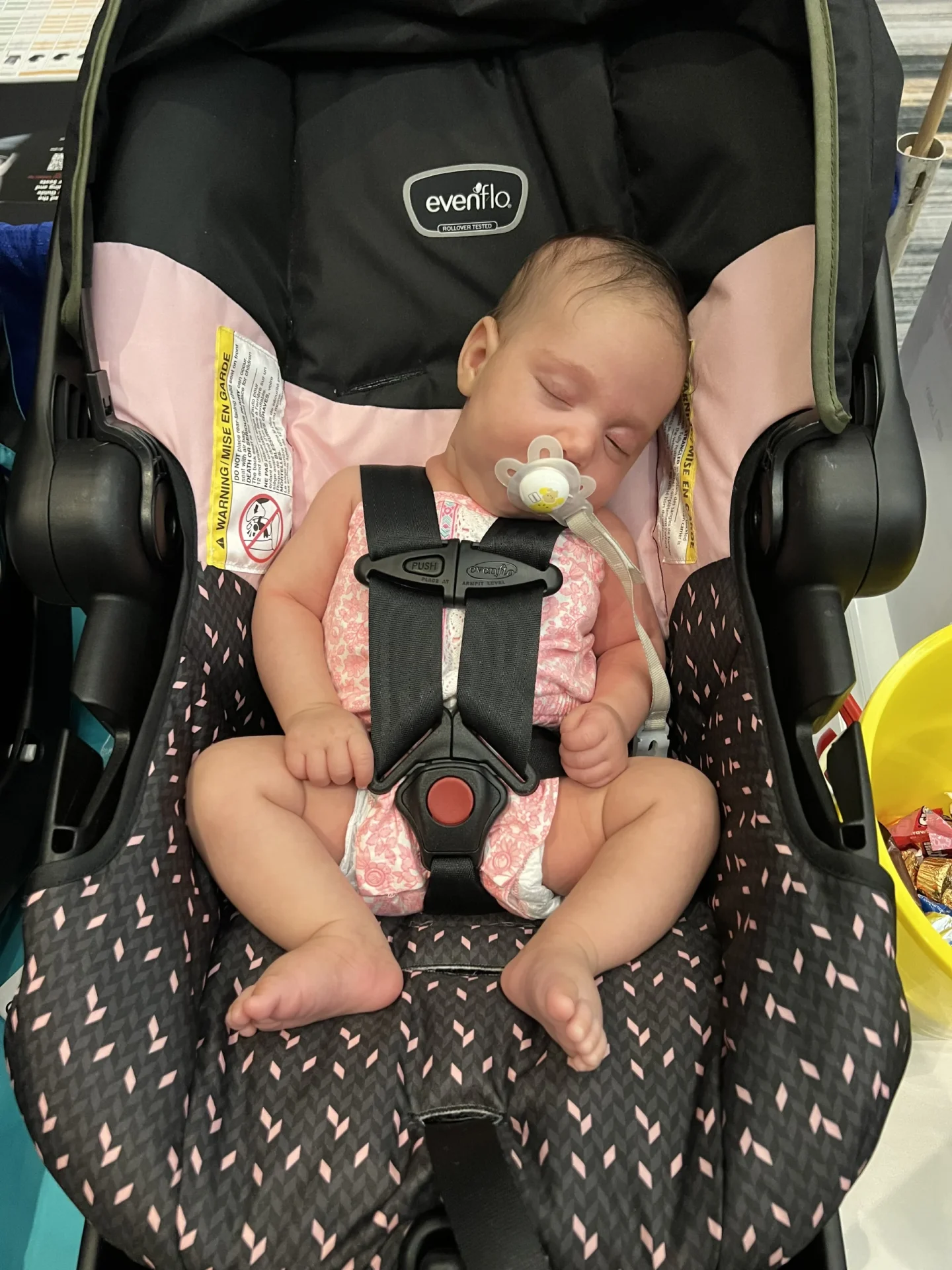 Sleeping newborn baby with pacifier securely buckled in a black and pink Evenflo NurtureMax infant car seat