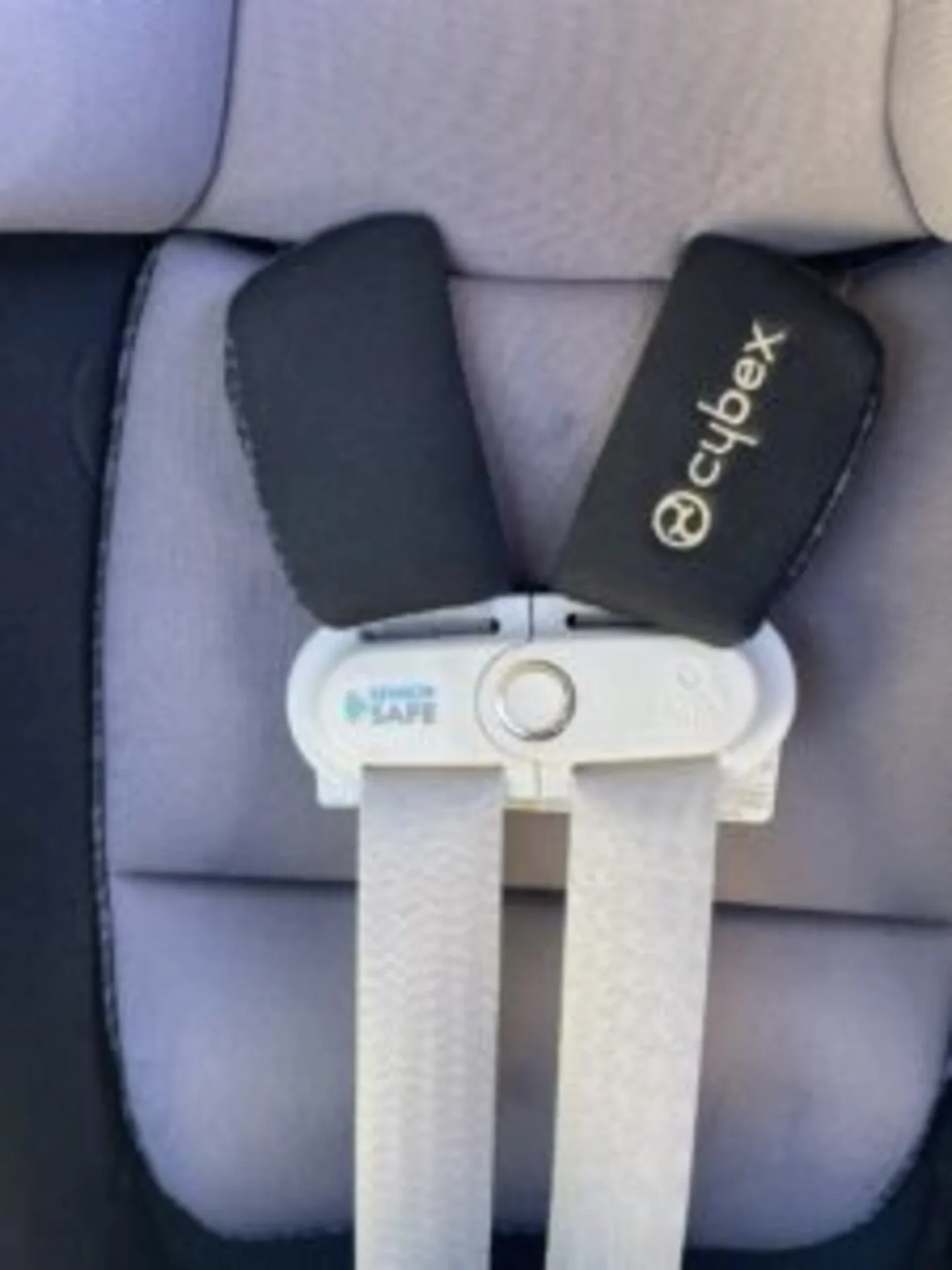 Cybex Sirona S child car seat harness with black padded shoulder straps, chest clip, and SensorSafe buckle on grey fabric sea