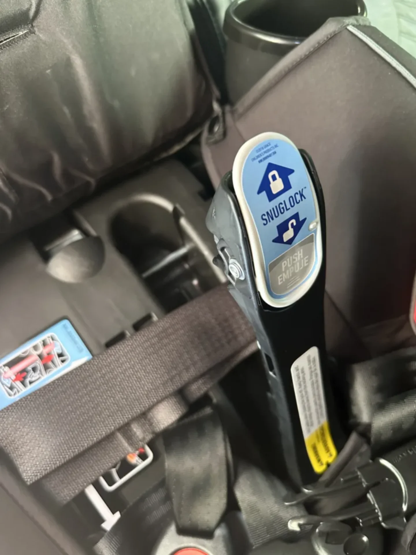 Graco TrioGrow SnugLock car seat buckle mechanism with blue push button label installed in vehicle back seat