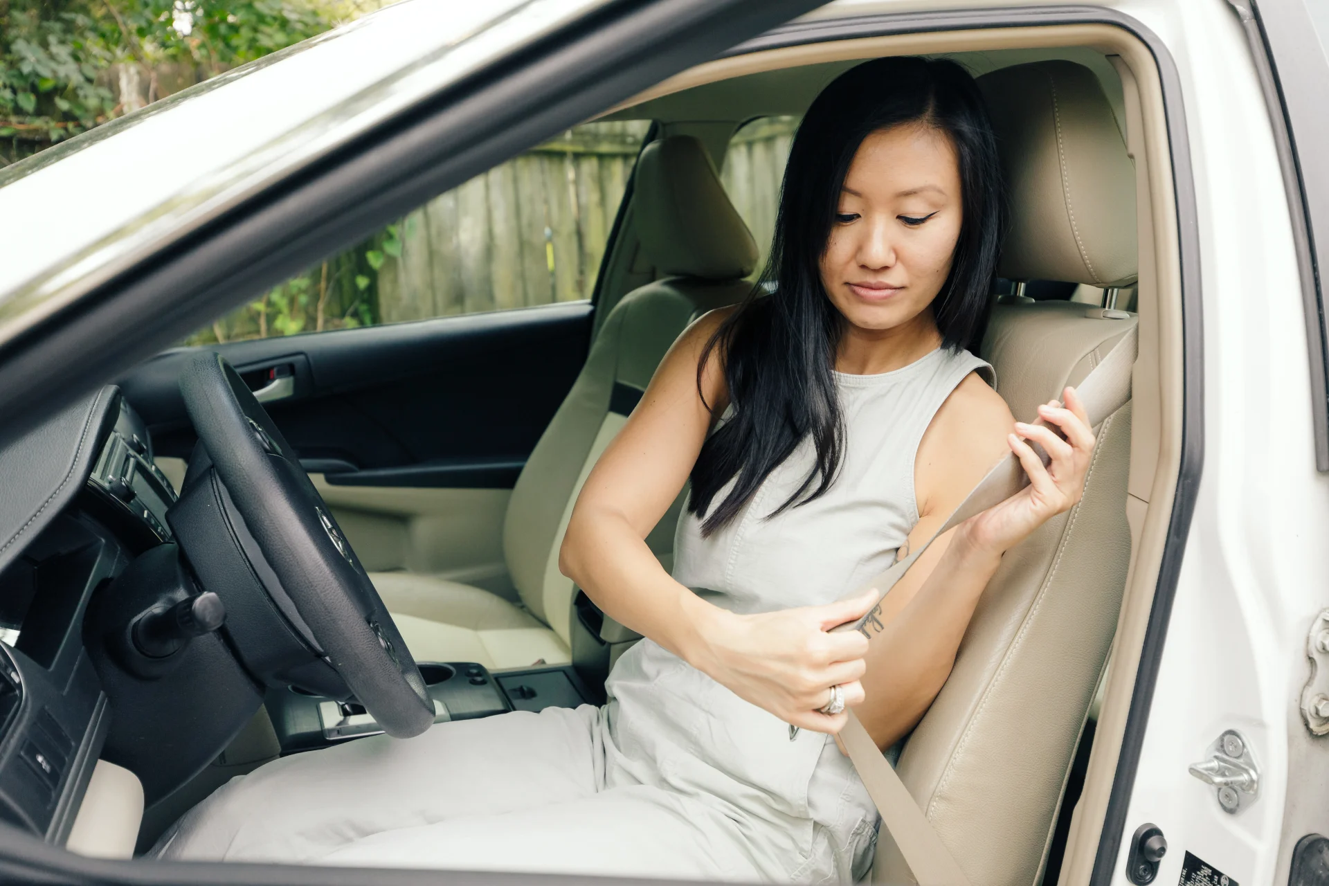 Young woman with long dark hair buckling her seatbelt in the driver seat of a white car with beige interior
