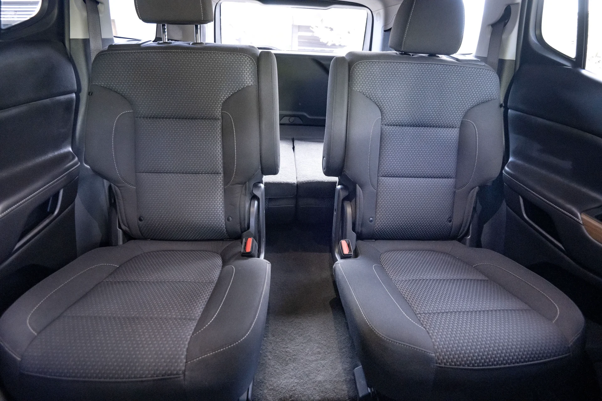 Clean gray carpet and fabric second-row captain's chairs in a car interior with visible red seatbelt buckles and textured uph