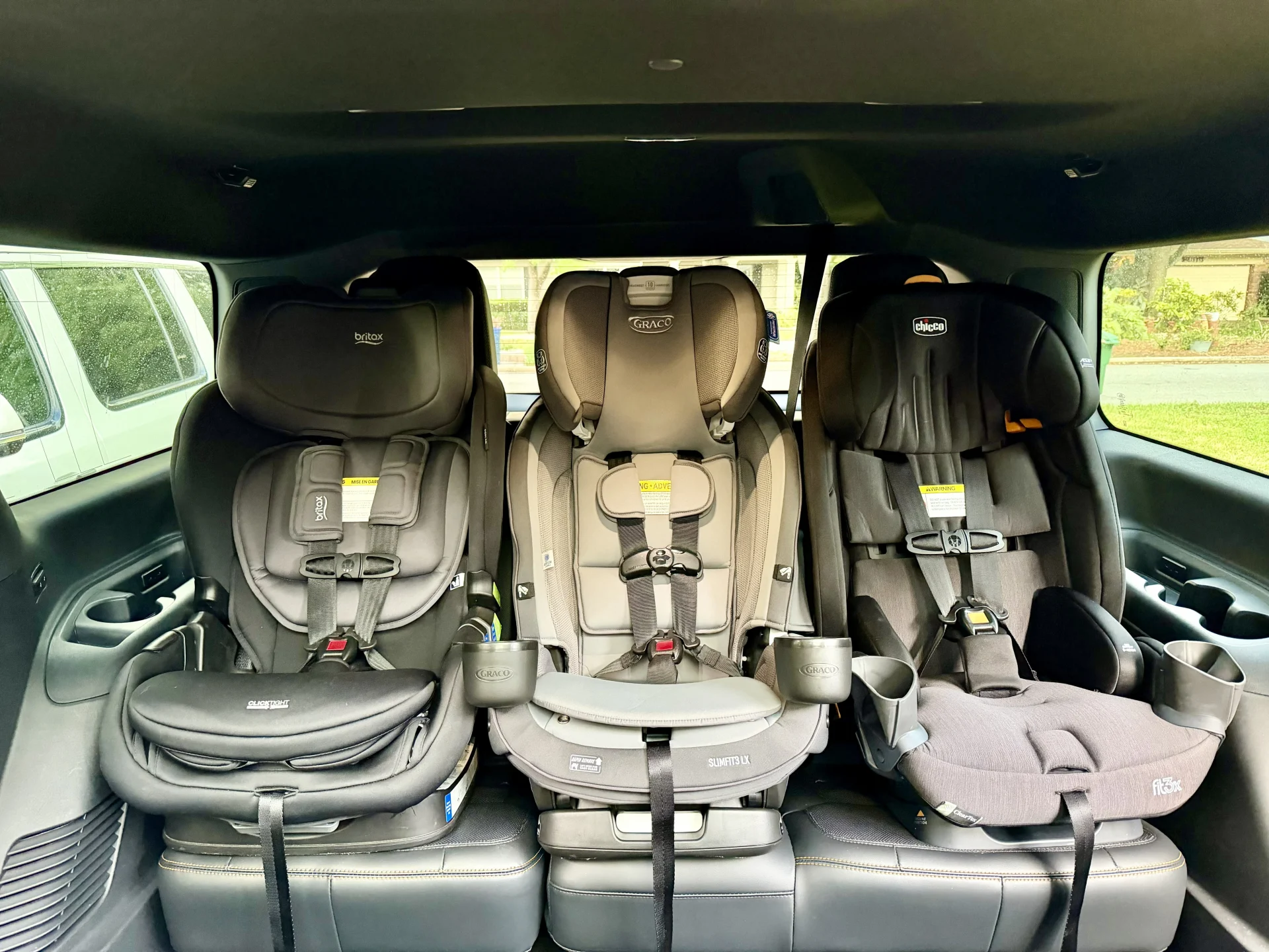 Three convertible car seats installed side by side in a minivan: black Britax, tan Graco SlimFit3 LX, and gray Chicco fitting