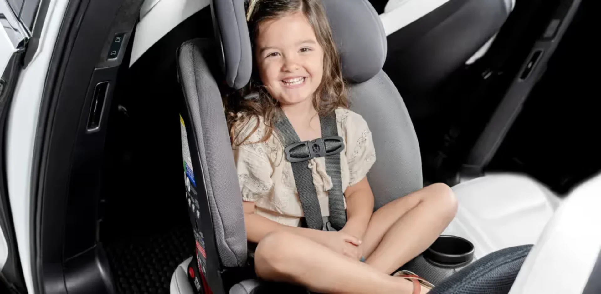 Happy young girl with brown hair smiling while safely buckled in a gray convertible car seat with five-point harness in a veh