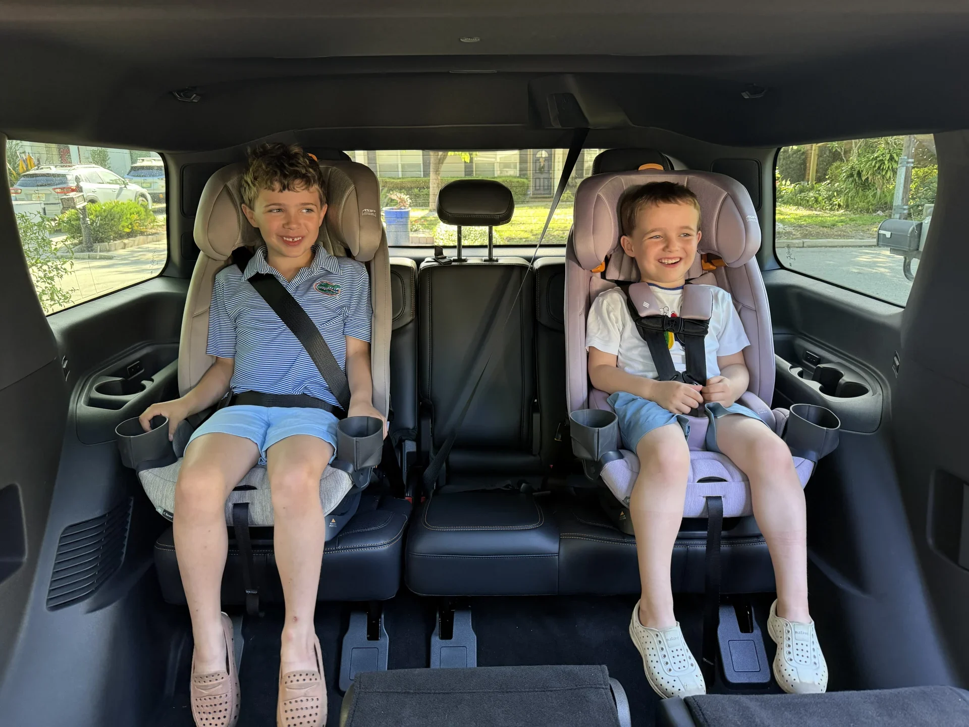 Chicco Fit3x Car Seats in SUV Backseat Two smiling boys buckled into Chicco Fit3x car seats in a spacious SUV backseat, one in forward-facing harness mode and one i