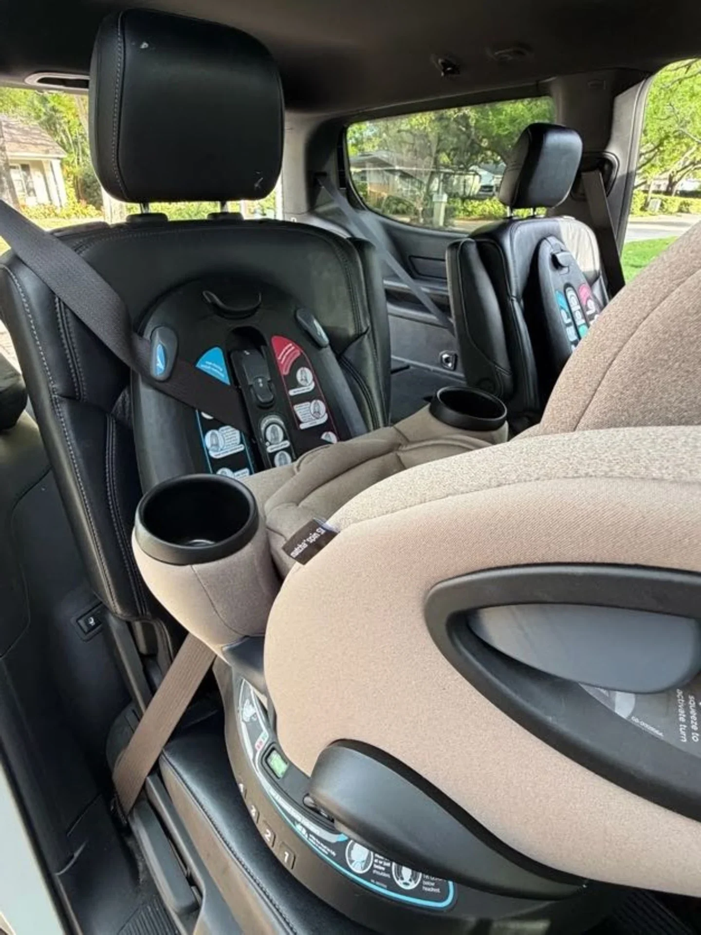 Joie Pepper vs Matcha Spin SI Side-by-Side Comparison Joie Pepper black rotating car seat and Matcha Spin SI beige car seat installed side by side in a black leather minivan inter