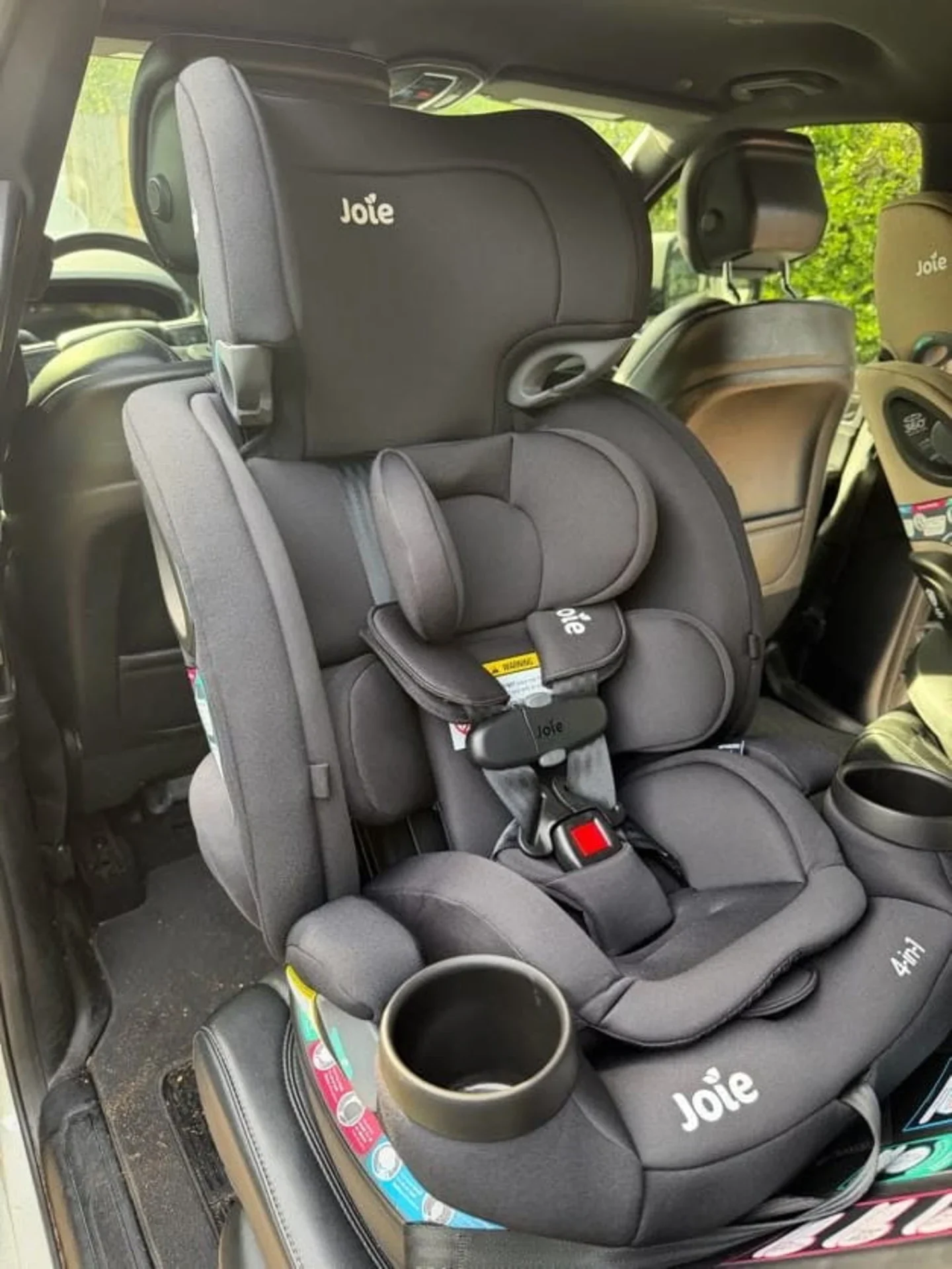 Joie Every Stage 4-in-1 Black Car Seat Installed Joie Every Stage 4-in-1 convertible car seat in black installed in car rear seat showing 5-point harness buckle and built-in