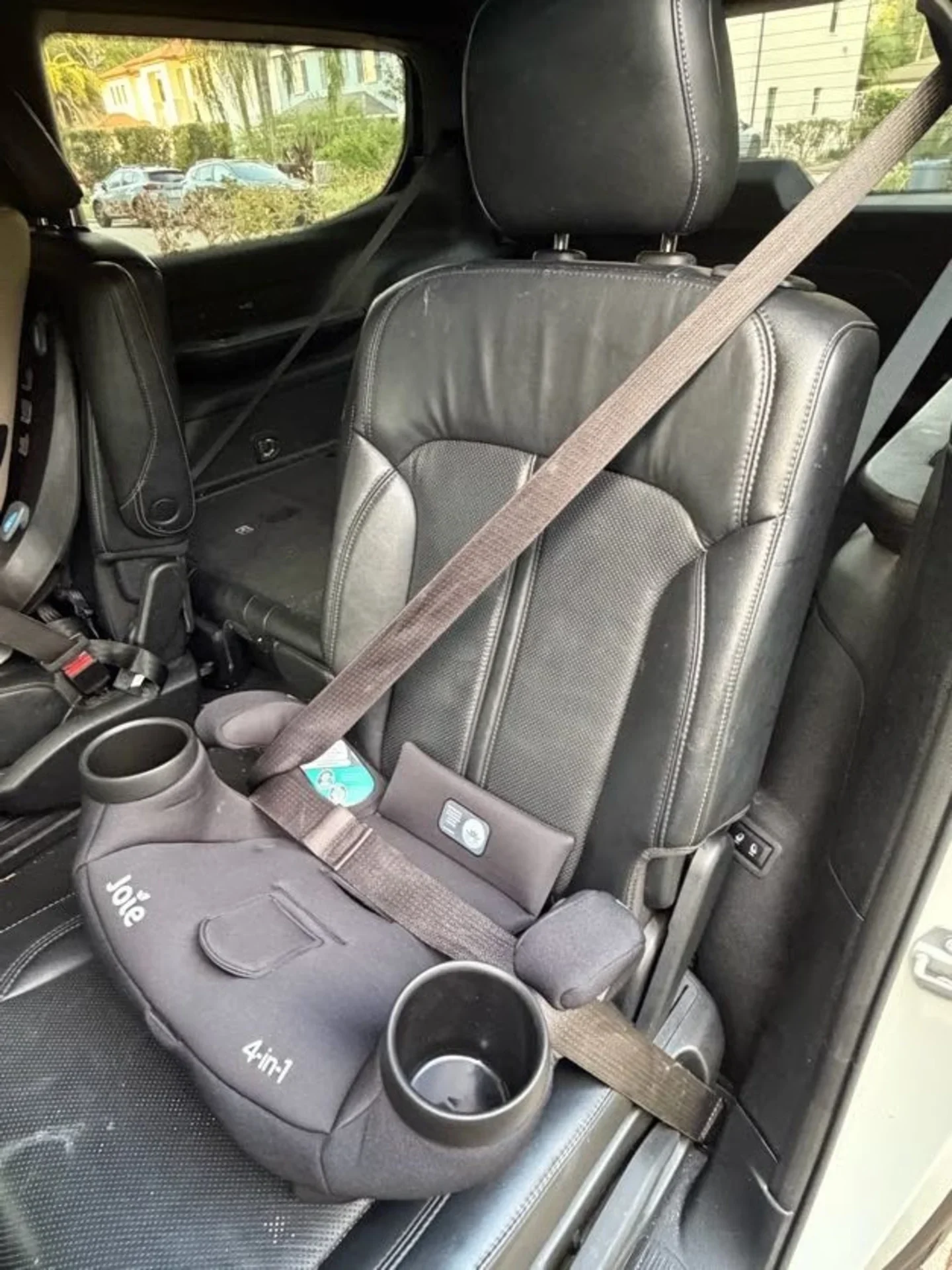 Joie 4-in-1 Child Booster Car Seat Installed Joie 4-in-1 rotating child car seat with dual cup holders secured by seatbelt on black leather rear vehicle seat