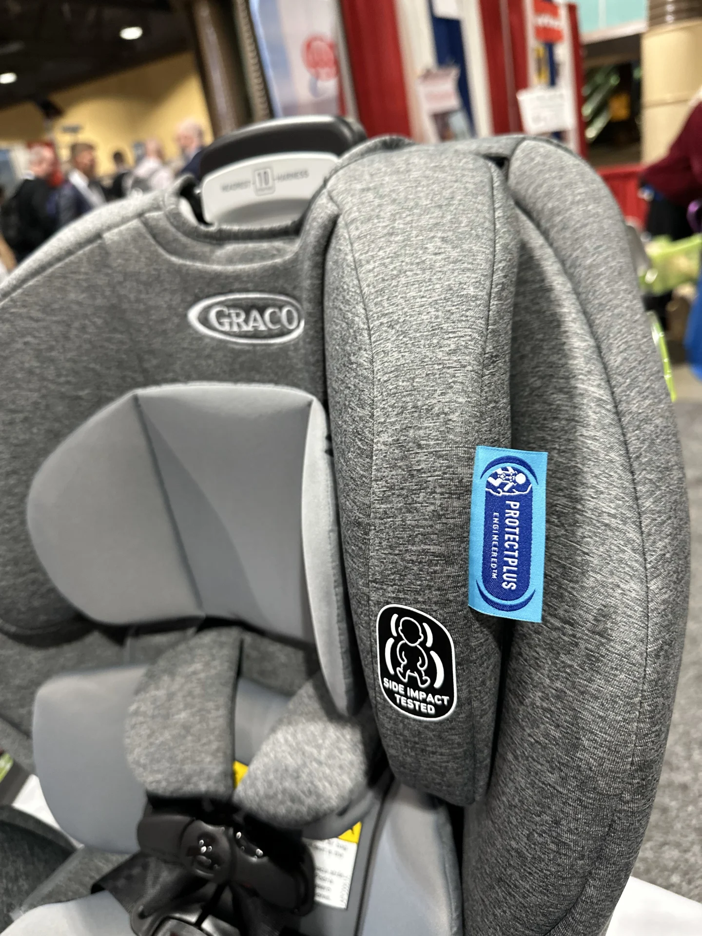 Close-up of a gray Graco car seat showing Side Impact Tested badge and ProtectPlus Engineered label on padded side wing